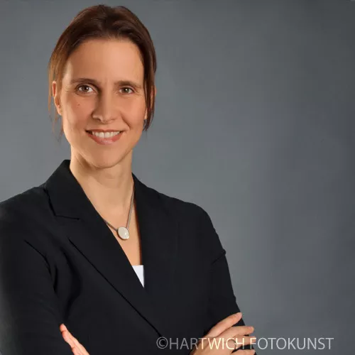 Professionelles Bewerbungsfoto einer Frau mit schulterlangem braunem Haar. Sie trägt einen dunklen Blazer über einem weißen Oberteil sowie eine dezente Halskette mit rundem Anhänger. Mit freundlichem Lächeln und aufrechter Haltung blickt sie selbstbewusst in die Kamera. Der Hintergrund ist neutral grau, passend für eine seriöse Darstellung. Professionelles Bewerbungsfoto einer Frau mit schulterlangem braunem Haar. Sie trägt einen dunklen Blazer über einem weißen Oberteil sowie eine dezente Halskette mit rundem Anhänger. Mit freundlichem Lächeln und aufrechter Haltung blickt sie selbstbewusst in die Kamera. Der Hintergrund ist neutral grau, passend für eine seriöse Darstellung.